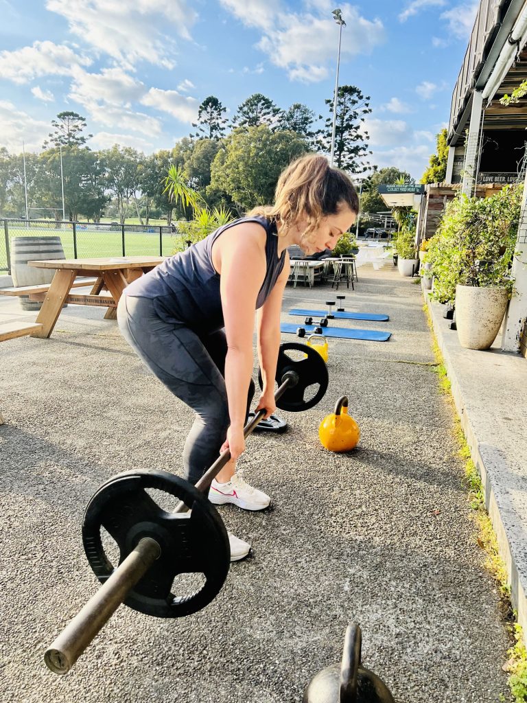 Woman deadlifting with guidance from a certified personal trainer